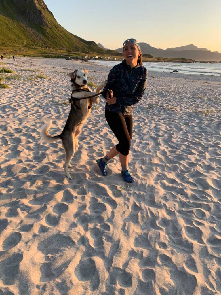 Woman and husky playing on a sandy beach in northern norway