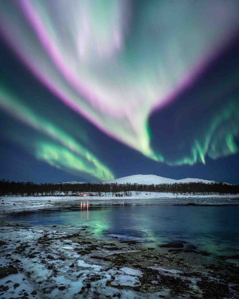 Fast-moving green and pink Northern Lights above snowy mountains near Tromsø