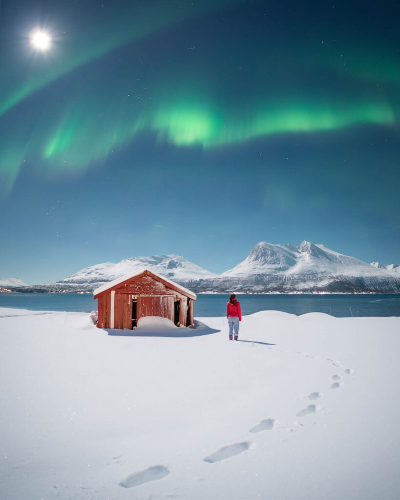 Northern Lights and full moon above a snowy landscape and mountains near Tromsø